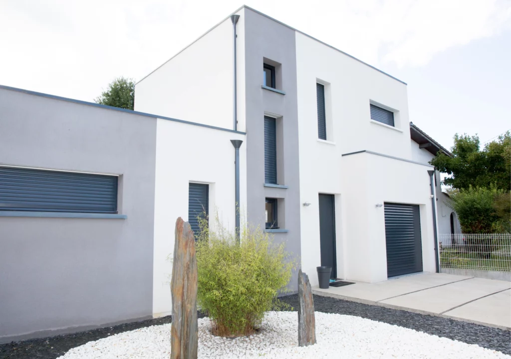 Modernes, weiß-graues Einfamilienhaus mit Garage und minimalistischer Gartenanlage mit weißen Steinen und drei senkrechten Steinen