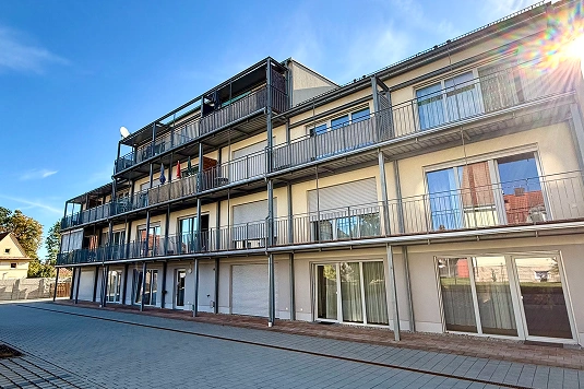 Dreistöckiges Wohngebäude mit Balkonen und großen Fenstern, Sonneneinstrahlung von rechts oben.